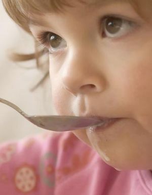 A young child feeds herself with a spoon
